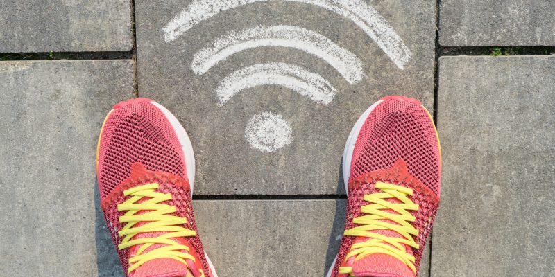 Wi-fi symbol on gray sidewalk with woman legs in sneakers, top view